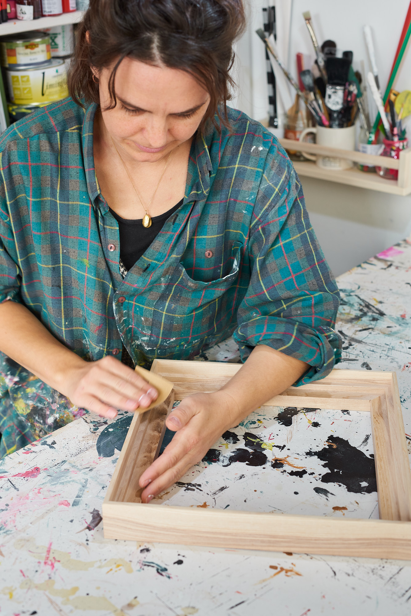 Closeup of framer wearing checked shirt sanding a wooden frame